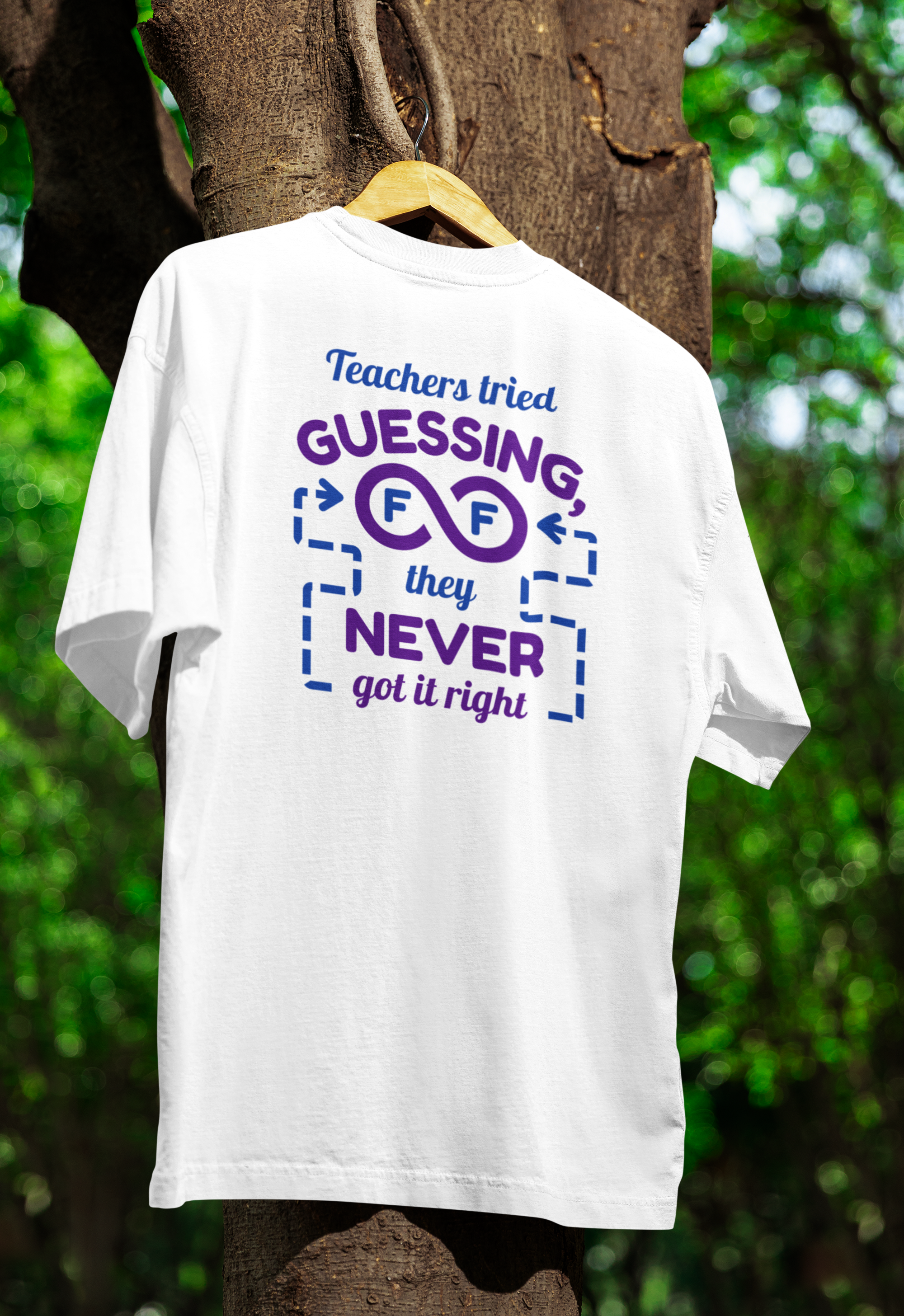 White t-shirt with humorous text design on a hanger against a tree and greenery background