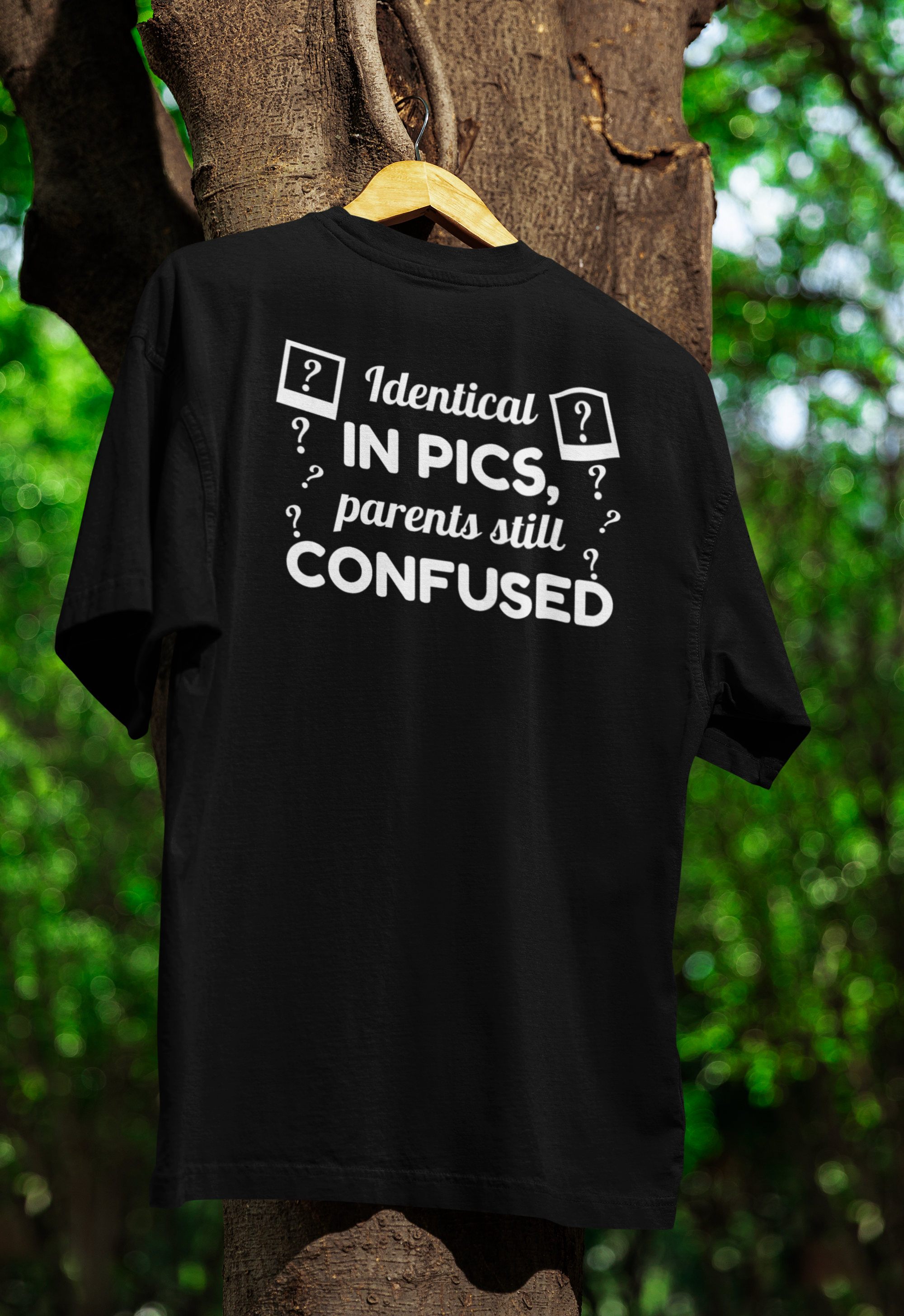 Black t-shirt for twins with humorous text design on a hanger against a natural background