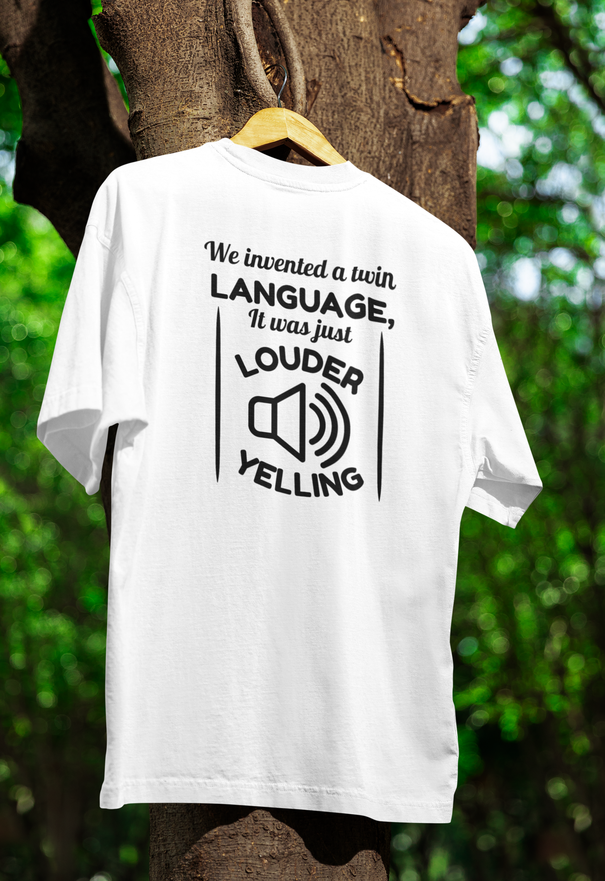 White t-shirt for twins with black text and graphic on a wooden hanger against a tree and green foliage background
