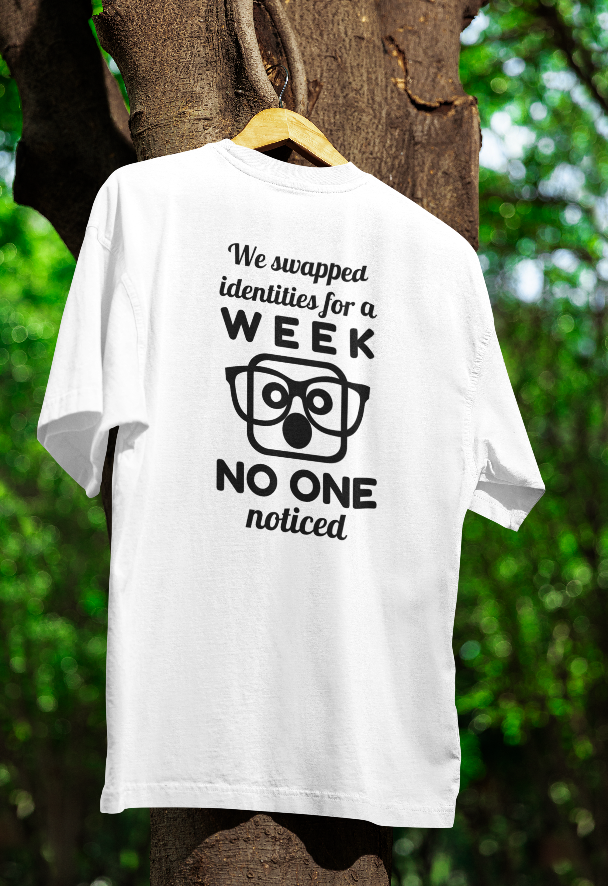 White t-shirt for twins with humorous text and graphic on a hanger against a tree and green foliage background