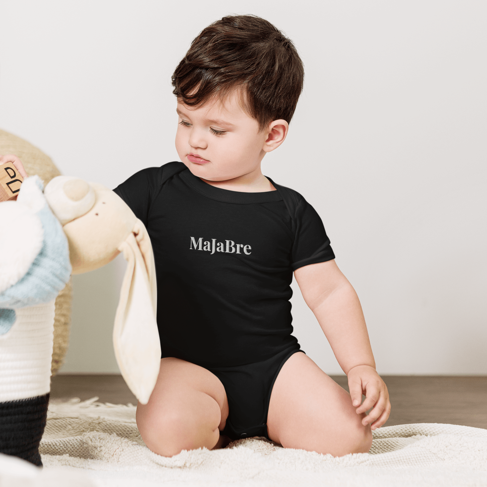 A toddler wearing black twin onesie with white majabre sign 